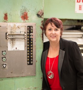 Nicole Stewart standing alongside one of the older pieces of equipment in her factory.