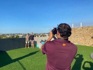 A man filming two men on a rooftop terrace.