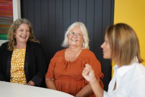 Three women talking to each other and smiling.