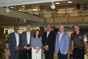 Group of six men and women standing together in corporate office.